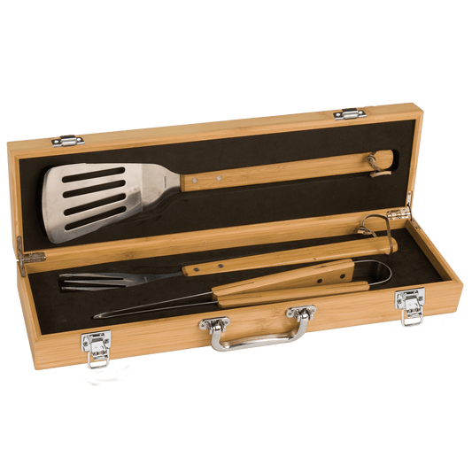 A 3-piece stainless steel BBQ tool set with bamboo handles, held inside a custom-engraved wooden storage case by charcoal colored foam.
