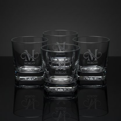 Four custom-engraved square heavy-base whiskey rocks glasses featuring a personalized monogram and name design (M with Morgan underneath), displayed together on a reflective surface