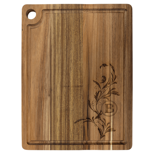 Rounded rectangular acacia wood cutting board with an integrated hanging hole, featuring a laser-engraved floral vine design surrounding the letter 'B'.