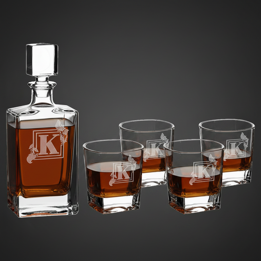 Engraved glass decanter and four matching square rocks glasses filled with amber liquid and personalized with a monogram logo on a dark background