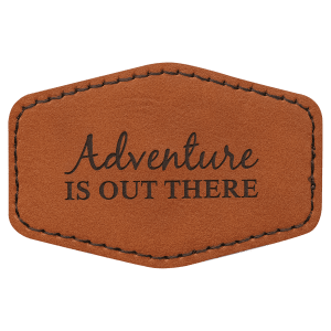 A brown leatherette hexagon patch with black stitched edges, featuring the text "Adventure IS OUT THERE" in a mix of script and block lettering.