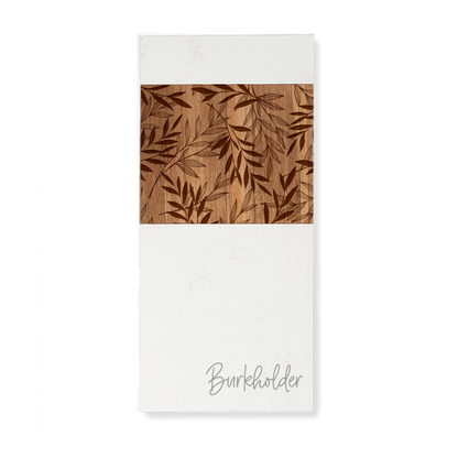 Custom engraved white marble and acacia wood serving board, enhanced with an engraved leaf design in the acacia wood panel, and personalized with the last name "Burkholder" in script on the white marble.