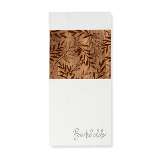 Custom engraved white marble and acacia wood serving board, enhanced with an engraved leaf design in the acacia wood panel, and personalized with the last name "Burkholder" in script on the white marble.