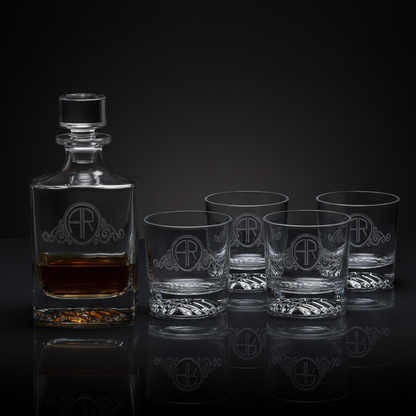 Clear glass decanter and four matching rocks glasses filled with amber liquid, featuring a custom monogram logo against a dark reflective surface