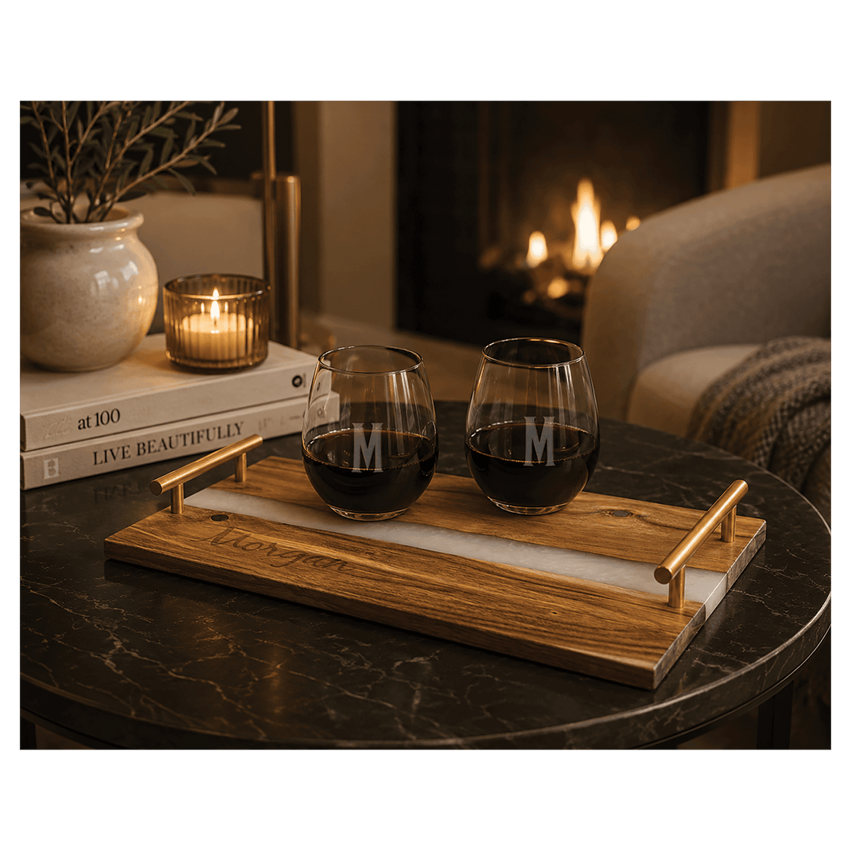 Custom engraved acacia wood serving tray with white pearl and blue resin river accent, gold handles, and two stemless wine glasses on a dark coffee table.