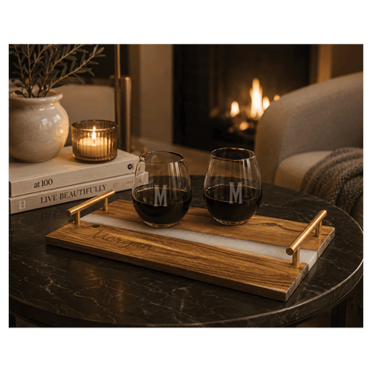Custom engraved acacia wood serving tray with white pearl and blue resin river accent, gold handles, and two stemless wine glasses on a dark coffee table.